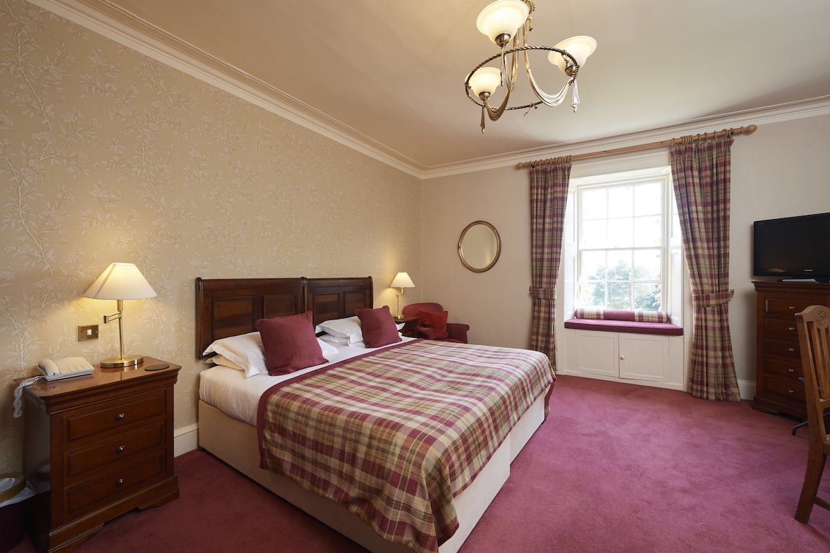 A neatly arranged bedroom with a large bed, bedside tables, a television, and a window with curtains.