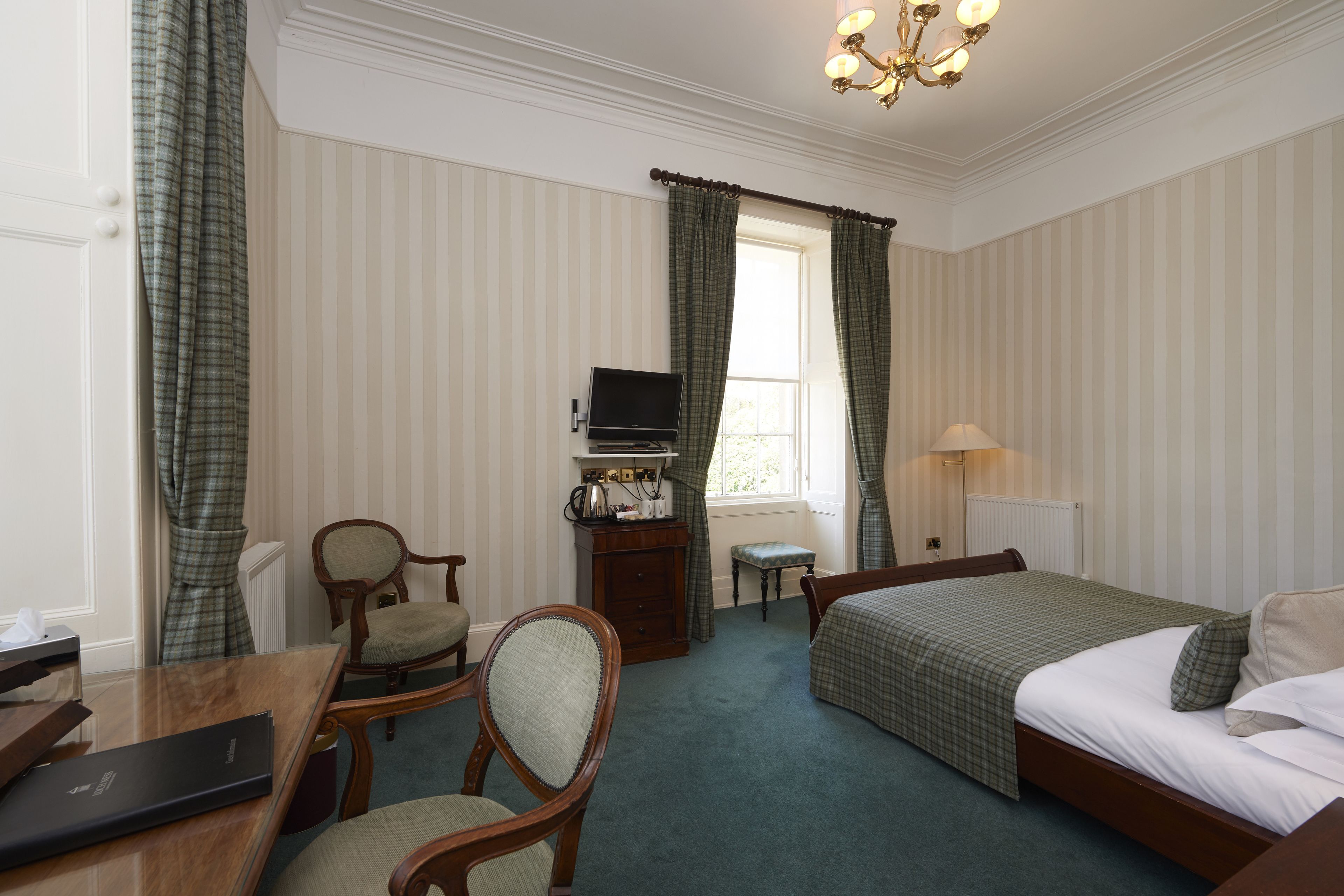Habitación de hotel con cama, escritorio, silla, televisión y ventana con cortinas.