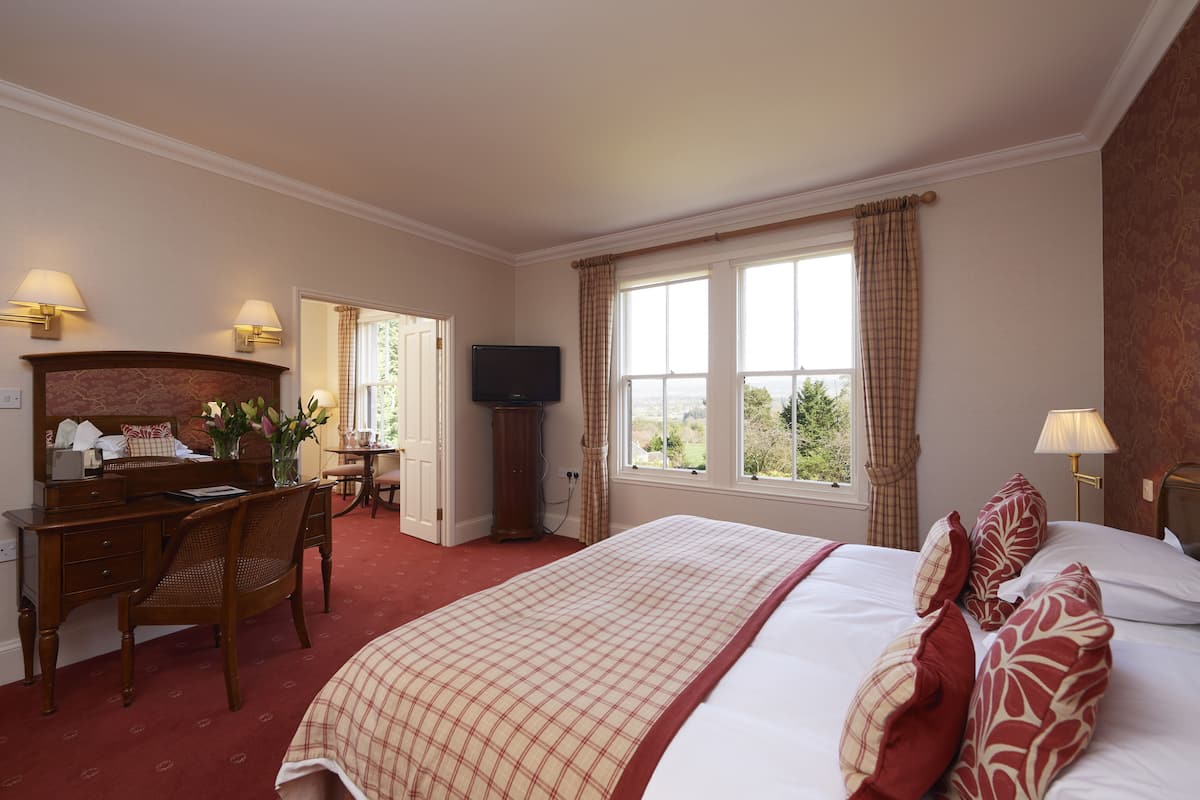 A hotel room with a large bed, a desk with a chair, a television, and a window with curtains.