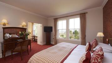 A hotel room with a large bed, a desk with a chair, a television, and a window with curtains.
