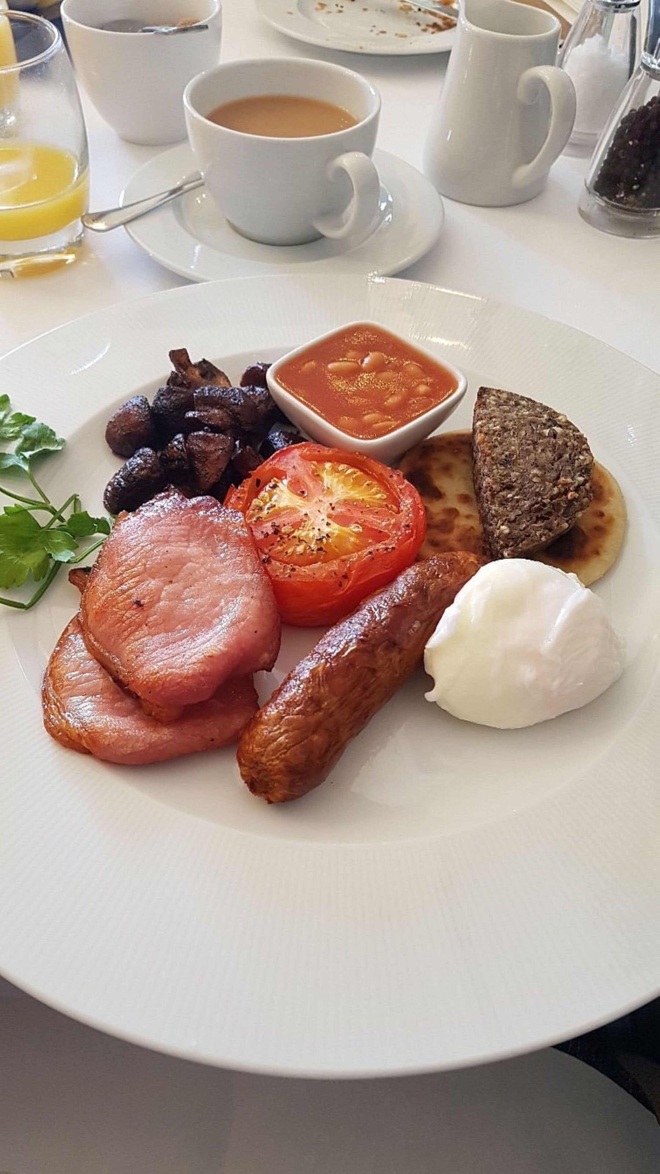 A breakfast plate with ham, sausages, tomato, and beans.