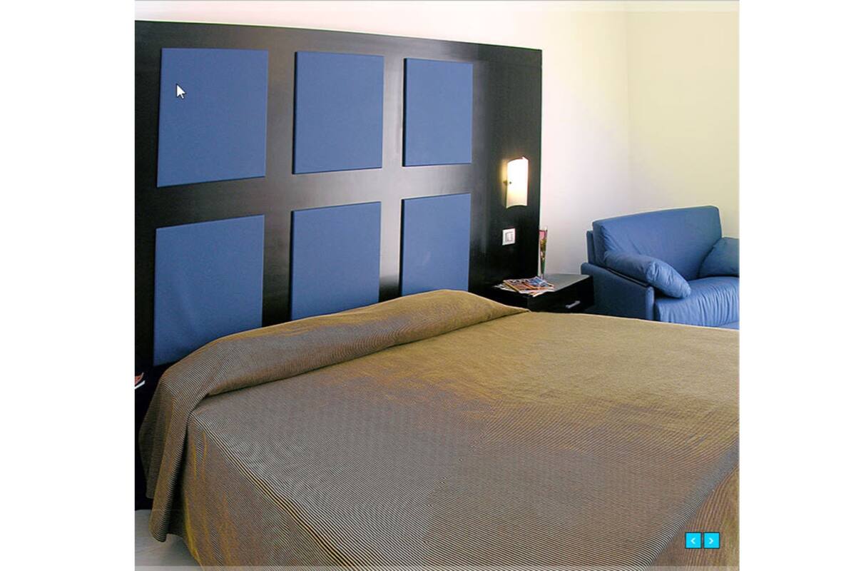 A hotel room with a large bed, a blue armchair, and a nightstand with a lamp.
