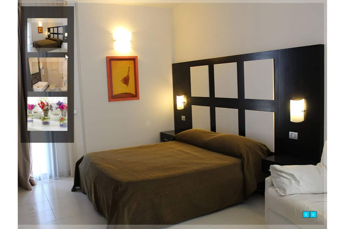 A hotel room with a bed, bedside tables, a wall-mounted light, and a framed picture.