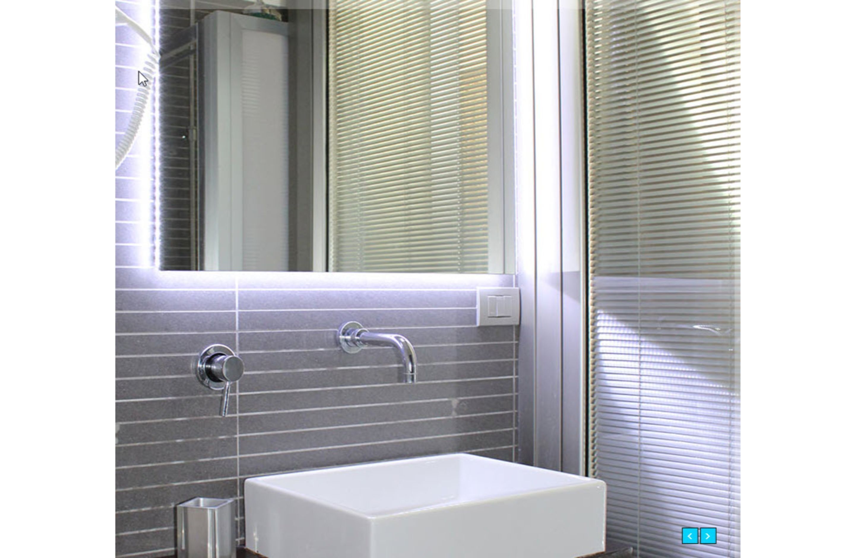 Un baño con lavamanos blanco, un espejo y una ventana con persianas.