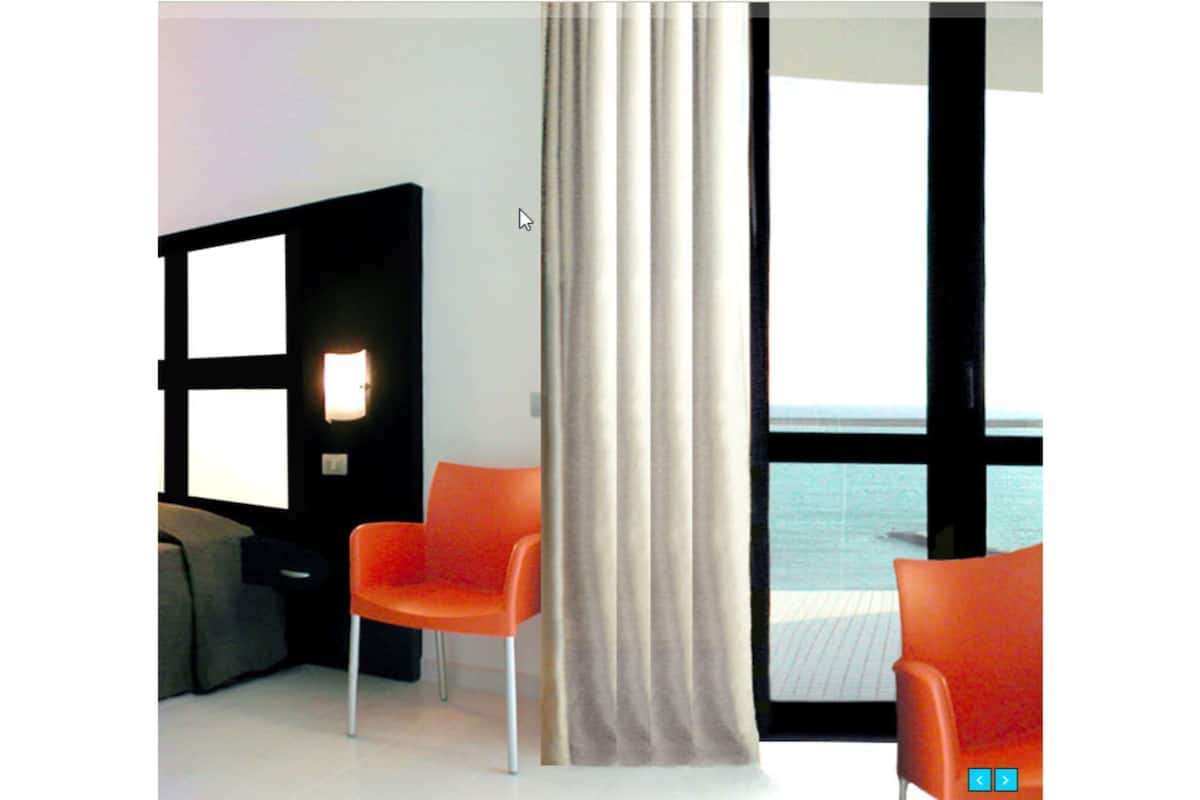 A room with two orange chairs, a large window with a view of the sea, and a curtain.