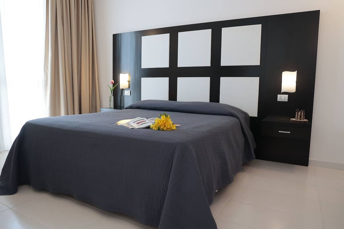 A modern bedroom with a large bed, a nightstand with a lamp, and a wall-mounted light fixture.