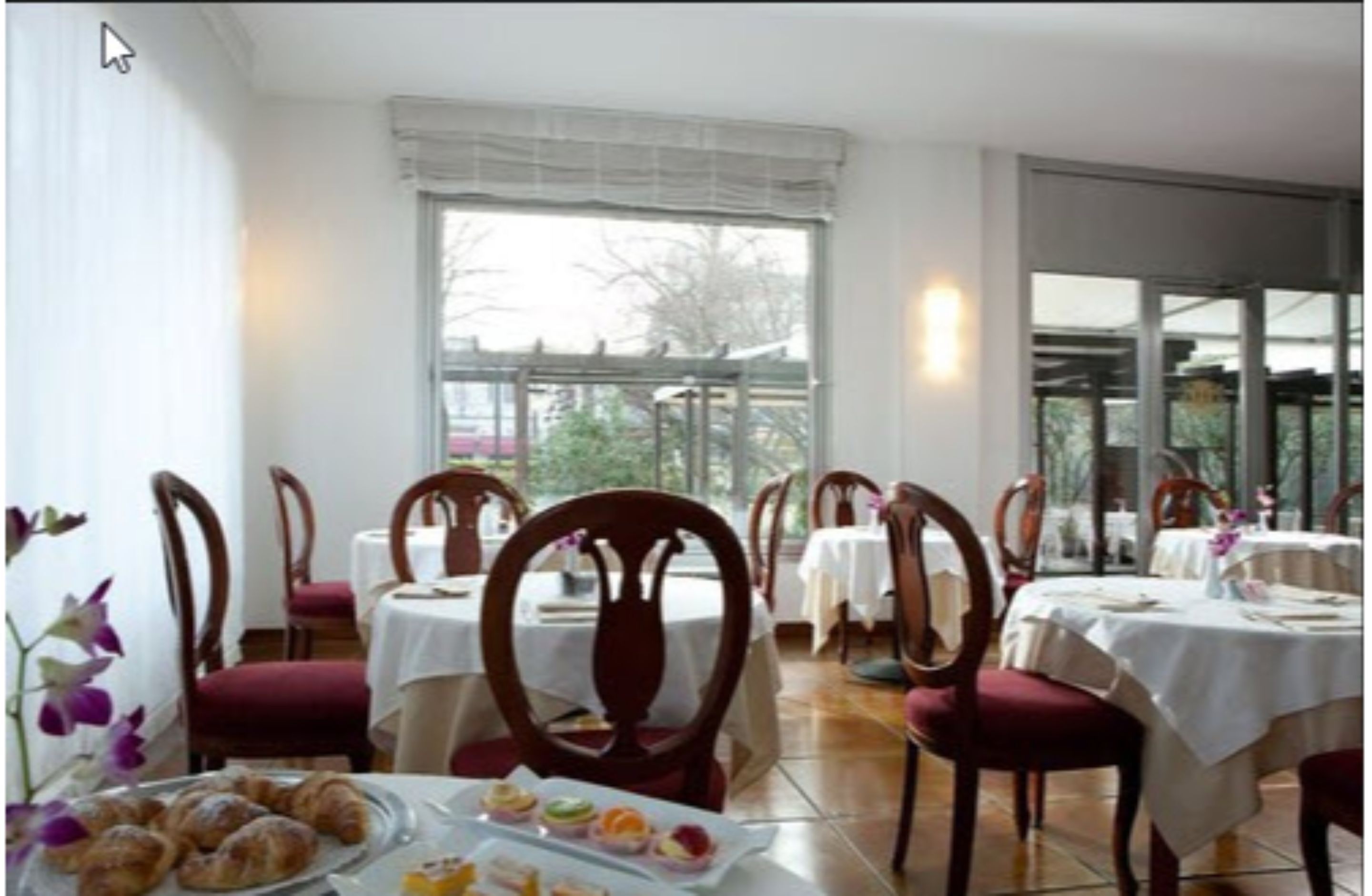 A dining area with tables and chairs, a window with a view, and a plate of pastries.