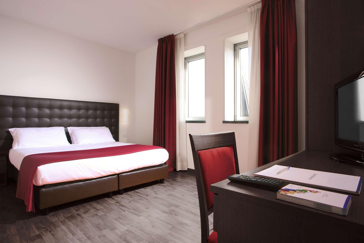 Une chambre d’hôtel comprenant un lit, un bureau avec un ordinateur, une chaise et un téléviseur.