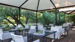 An outdoor patio with tables and wicker chairs, surrounded by greenery and trees. - Best Western Park Hotel Continental (San Dona di Piave)