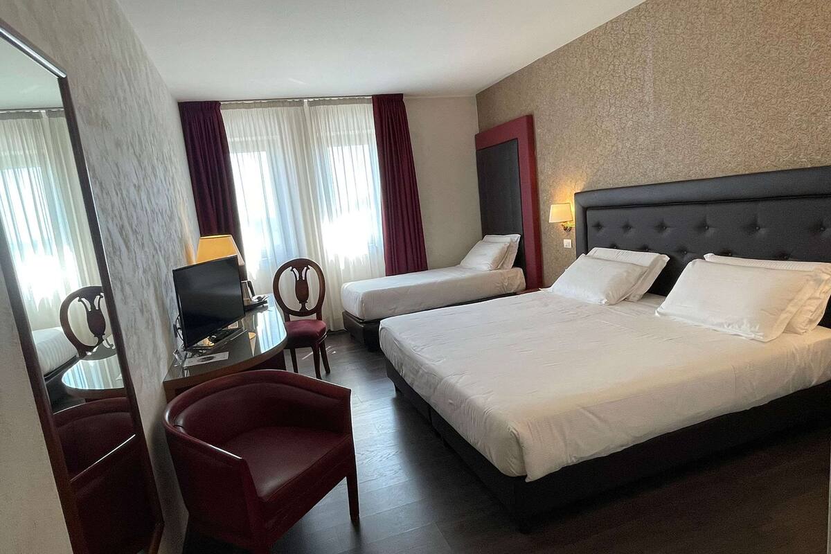 A hotel room with a large bed, a smaller bed, a desk with a chair, and a TV.