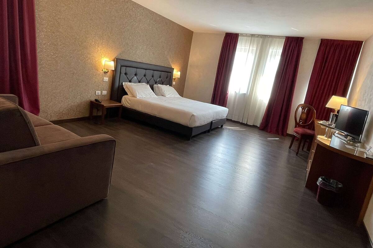 A hotel room with a bed, a desk with a computer, a chair, and a sofa.