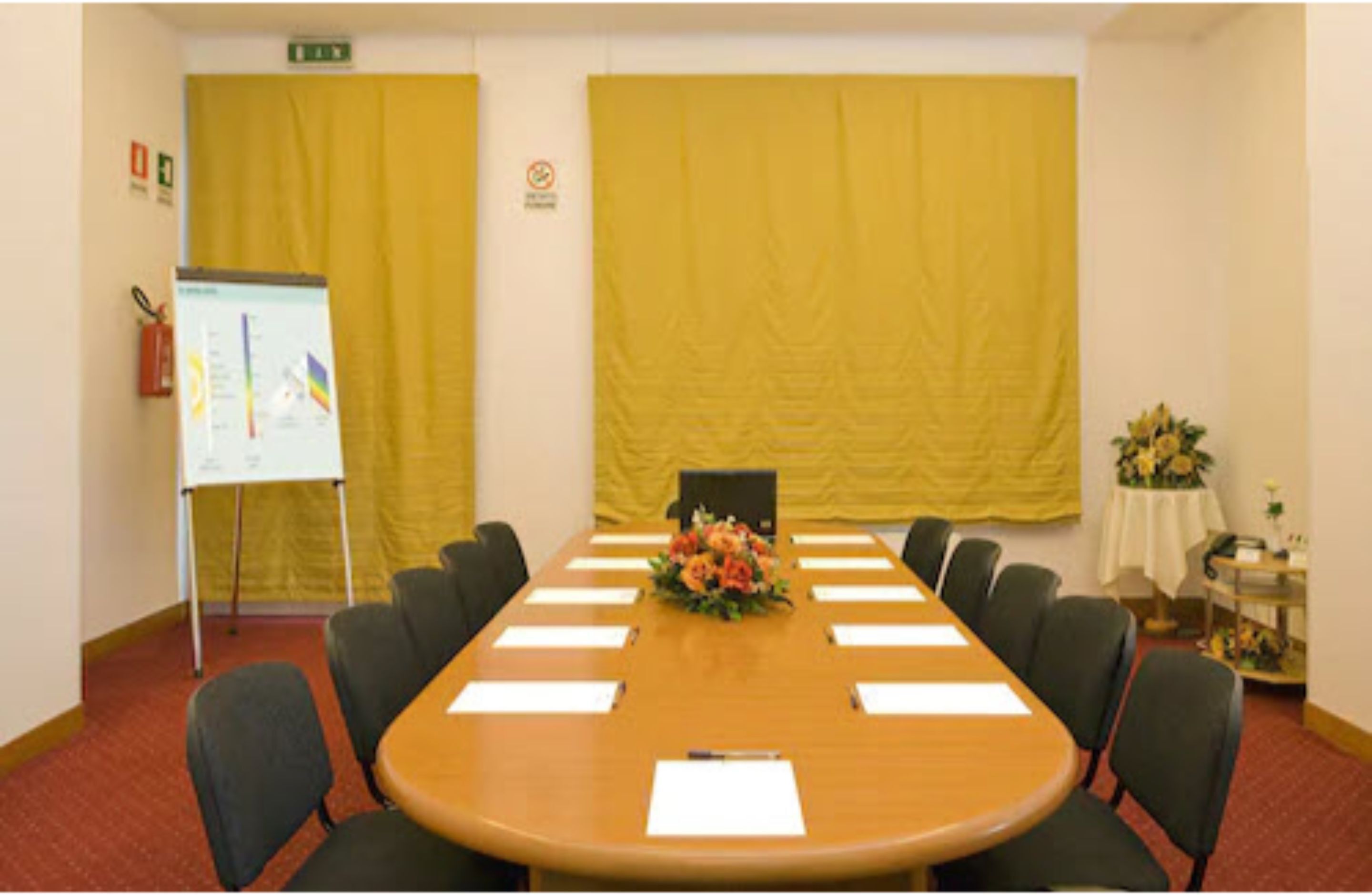 A conference room with a long table, black chairs, a whiteboard, and yellow curtains.