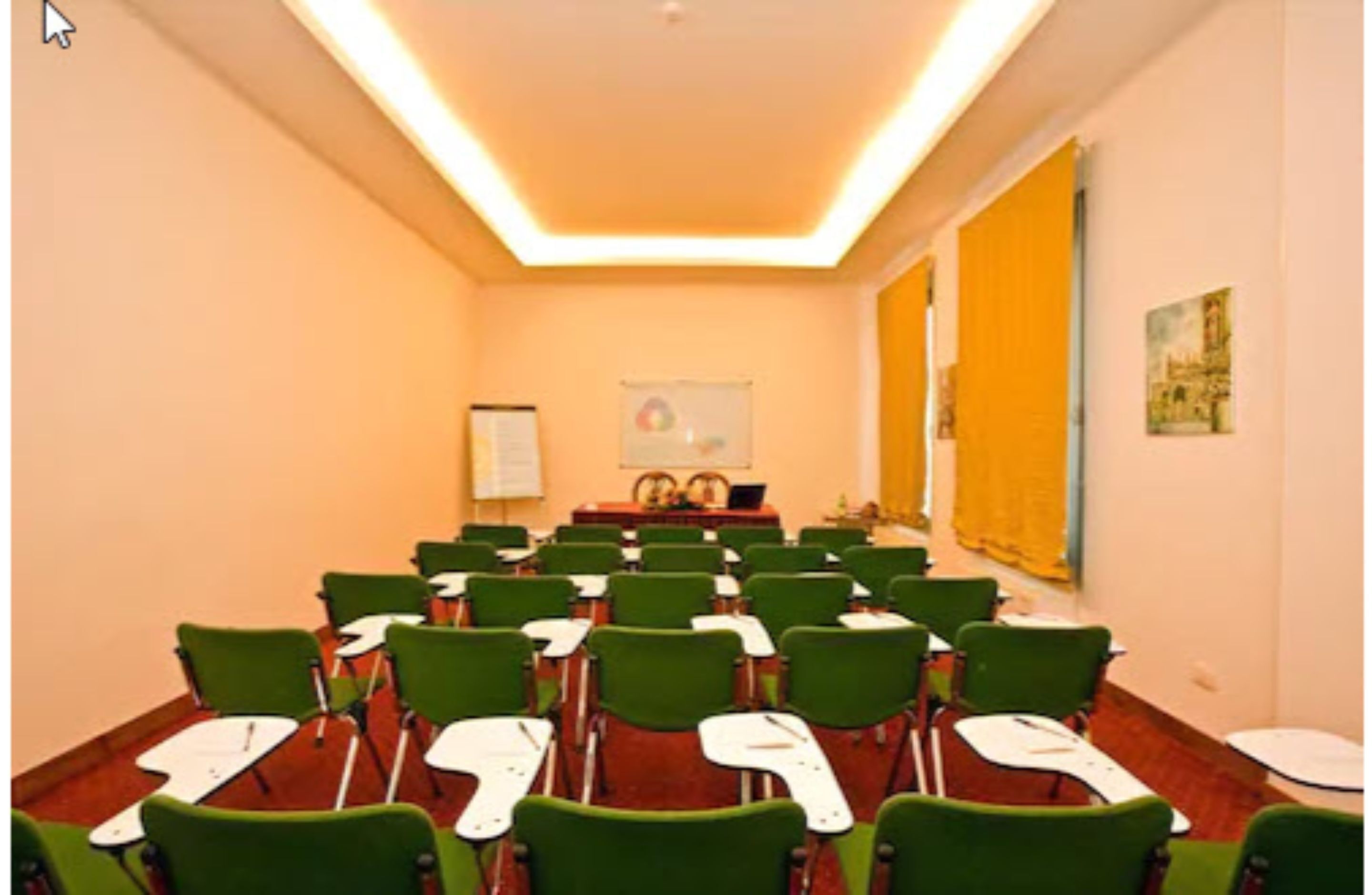 Une salle de classe avec des chaises et des tables vertes, un tableau blanc et un écran de projection.