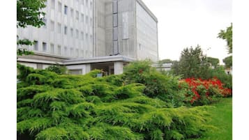 Ein modernes Hotel mit Glasfassade, umgeben von üppigem Grün und roten Blüten.