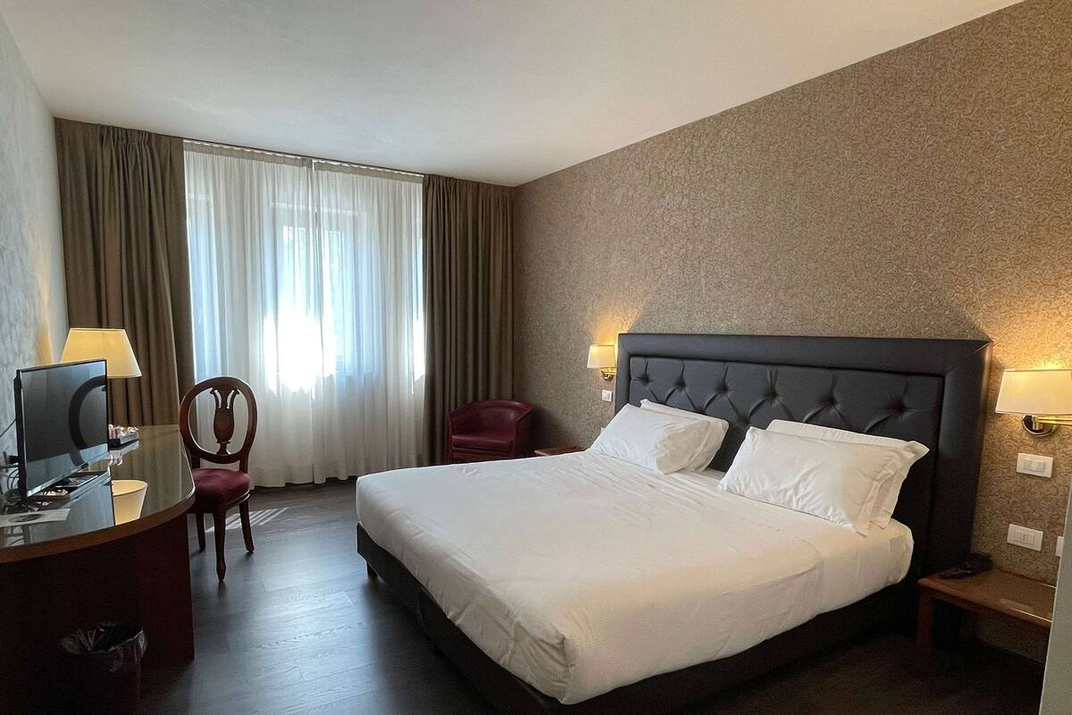 A hotel room with a large bed, a desk with a computer, a chair, and a TV.