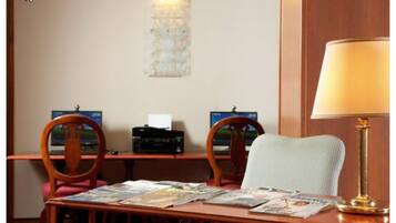 Una camera d'albergo con una scrivania in legno, due sedie, una lampada e un'opera d'arte appesa al muro.