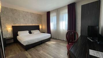 Ein Hotelzimmer mit Bett, Schreibtisch, Sessel und Fernseher.