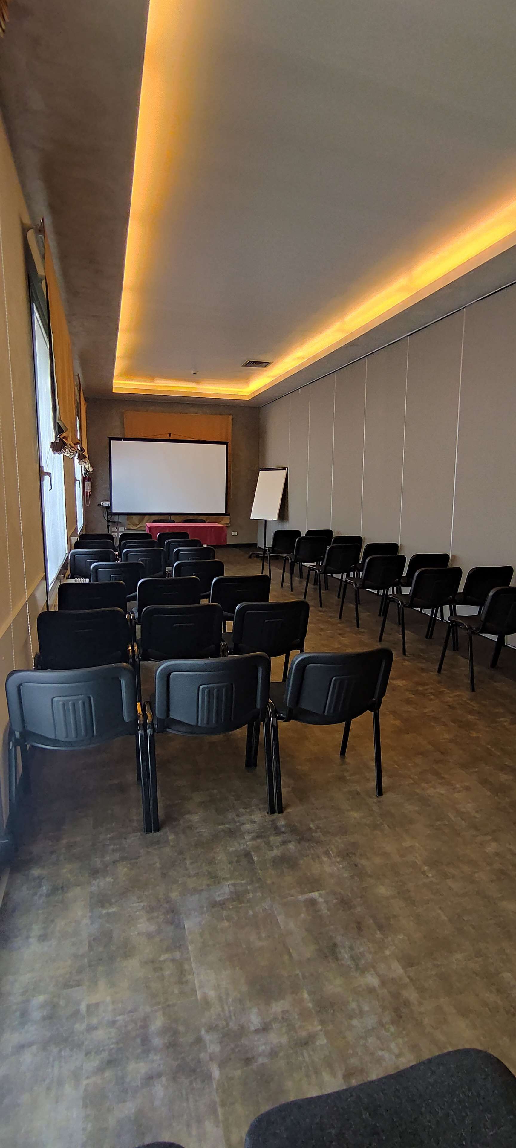 A conference room with rows of black chairs, a whiteboard, and a projector screen.