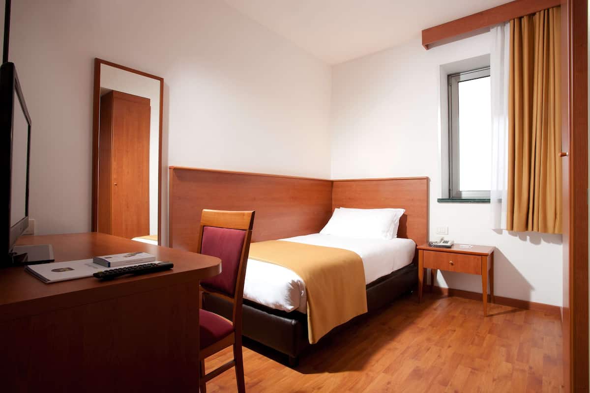A hotel room with a bed, a desk, a chair, a nightstand, and a window with curtains.