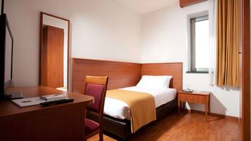 Une chambre d’hôtel avec un lit, un bureau, une chaise, une table de chevet et une fenêtre avec des rideaux.