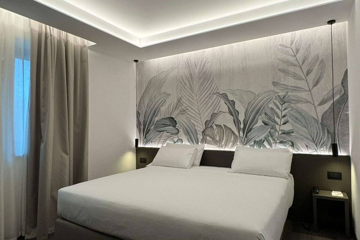 A modern bedroom with a large bed, a headboard with a leaf pattern, and a nightstand with a lamp.