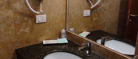 Un baño con lavamanos de encimera de granito, dos secadores de pelo montados en la pared y un espejo grande.
