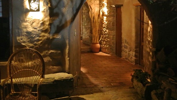 A stone-walled corridor with a rustic wooden bench and a chair, leading to a door. - Refugio Del Pintor (Tilcara)