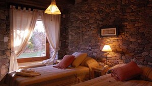 A cozy room with two beds, a stone wall, and a window with curtains. - Refugio Del Pintor (Tilcara)