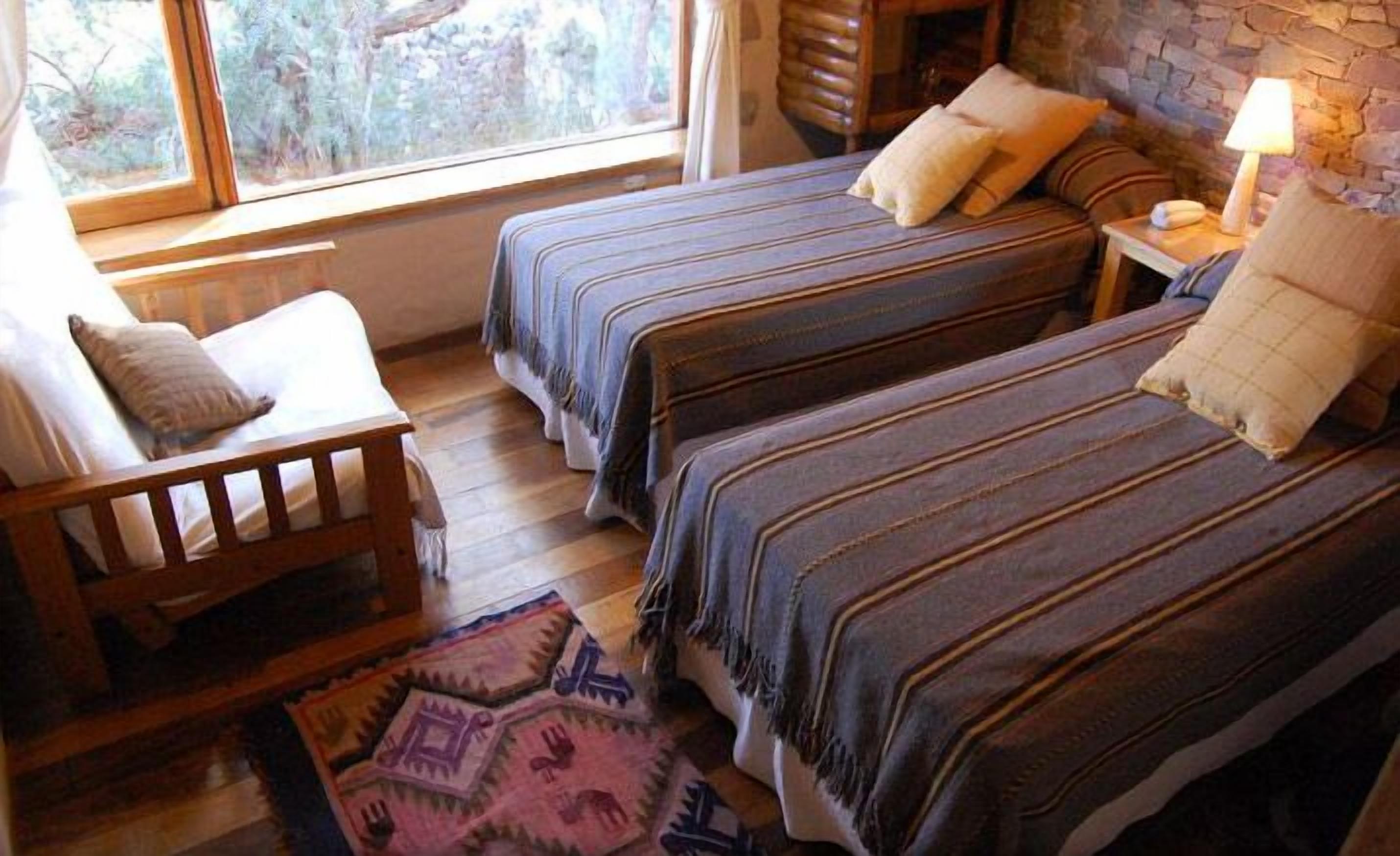 Una habitación acogedora con dos camas, una silla de madera, una mesita de noche y una lámpara.