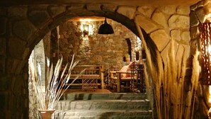 A stone-walled room with a rustic ambiance, featuring a wooden bench, a potted plant, and a bell hanging from the ceiling. - Refugio Del Pintor (Tilcara)