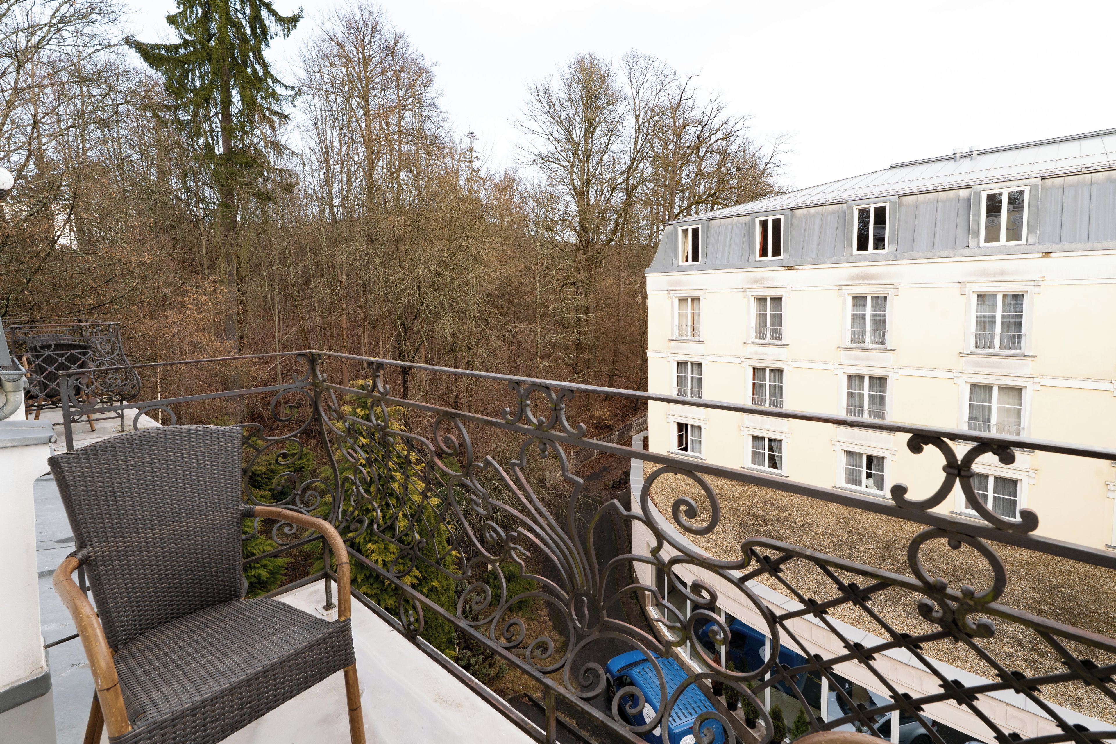 A balcony with a wicker chair, a metal railing, and a view of a building with multiple windows.