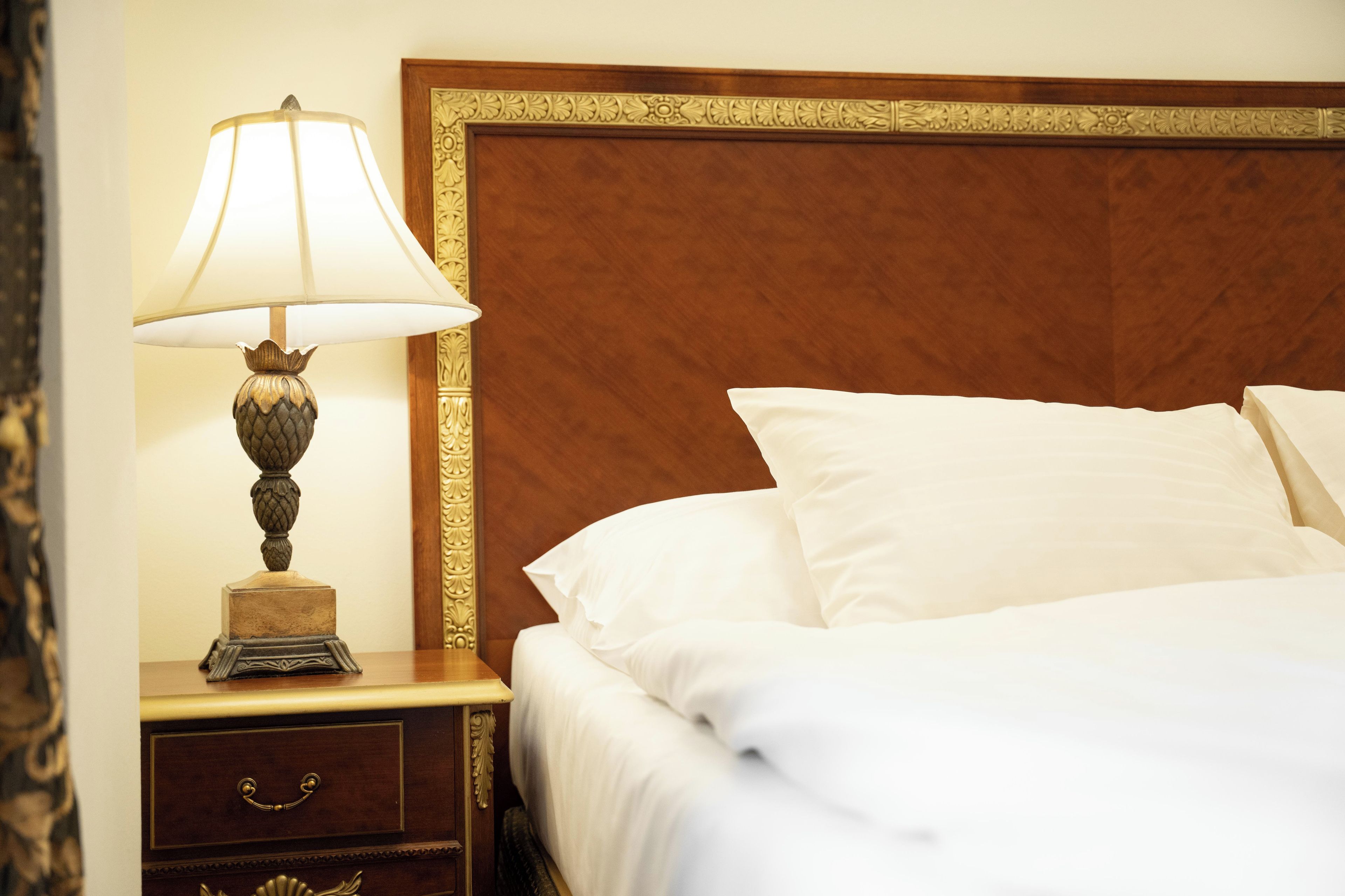 A neatly made bed with white linens, a wooden nightstand with a lamp, and a decorative headboard.