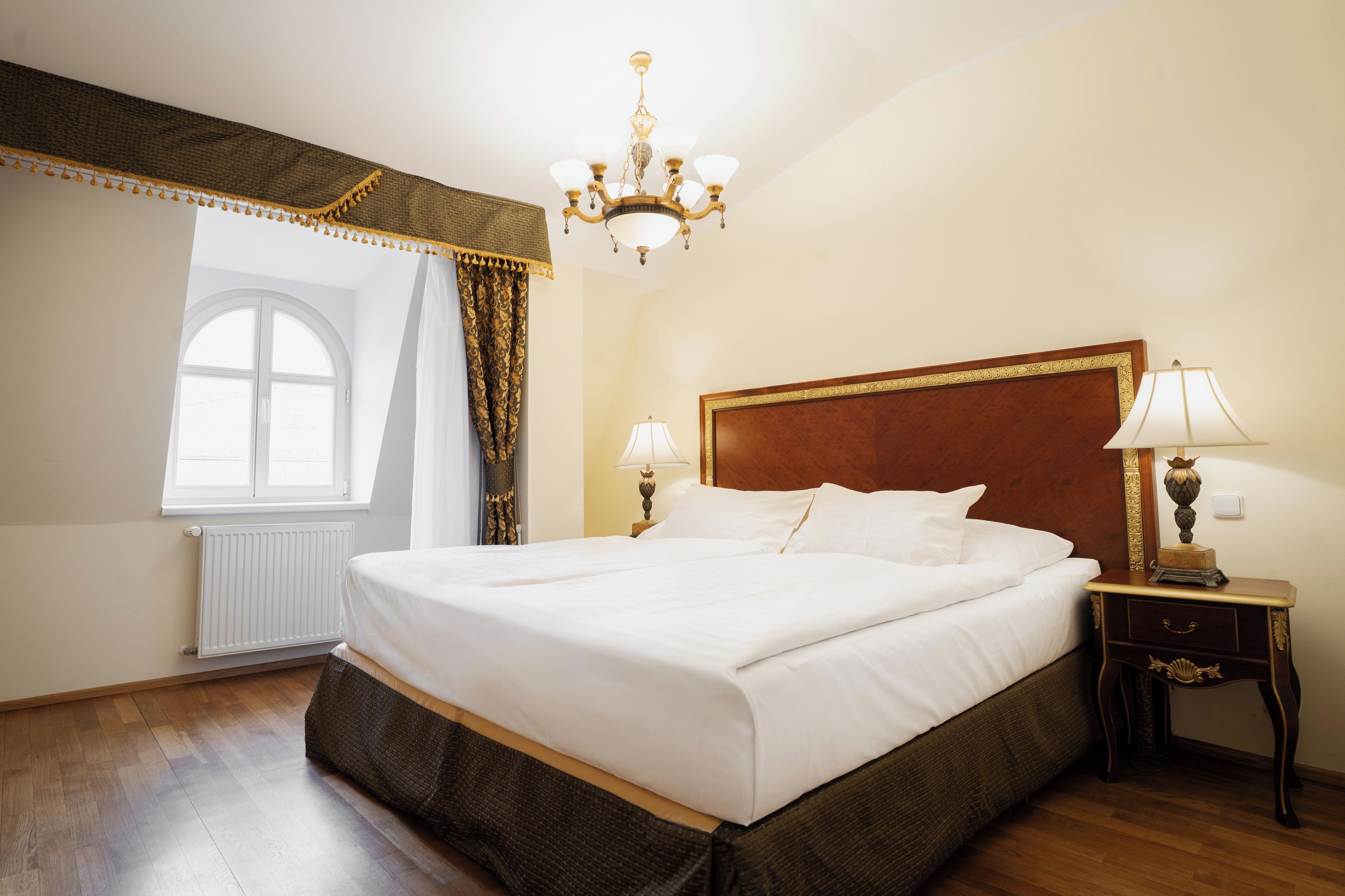 A hotel room with a large bed, two bedside lamps, a chandelier, and a view of the outdoors.