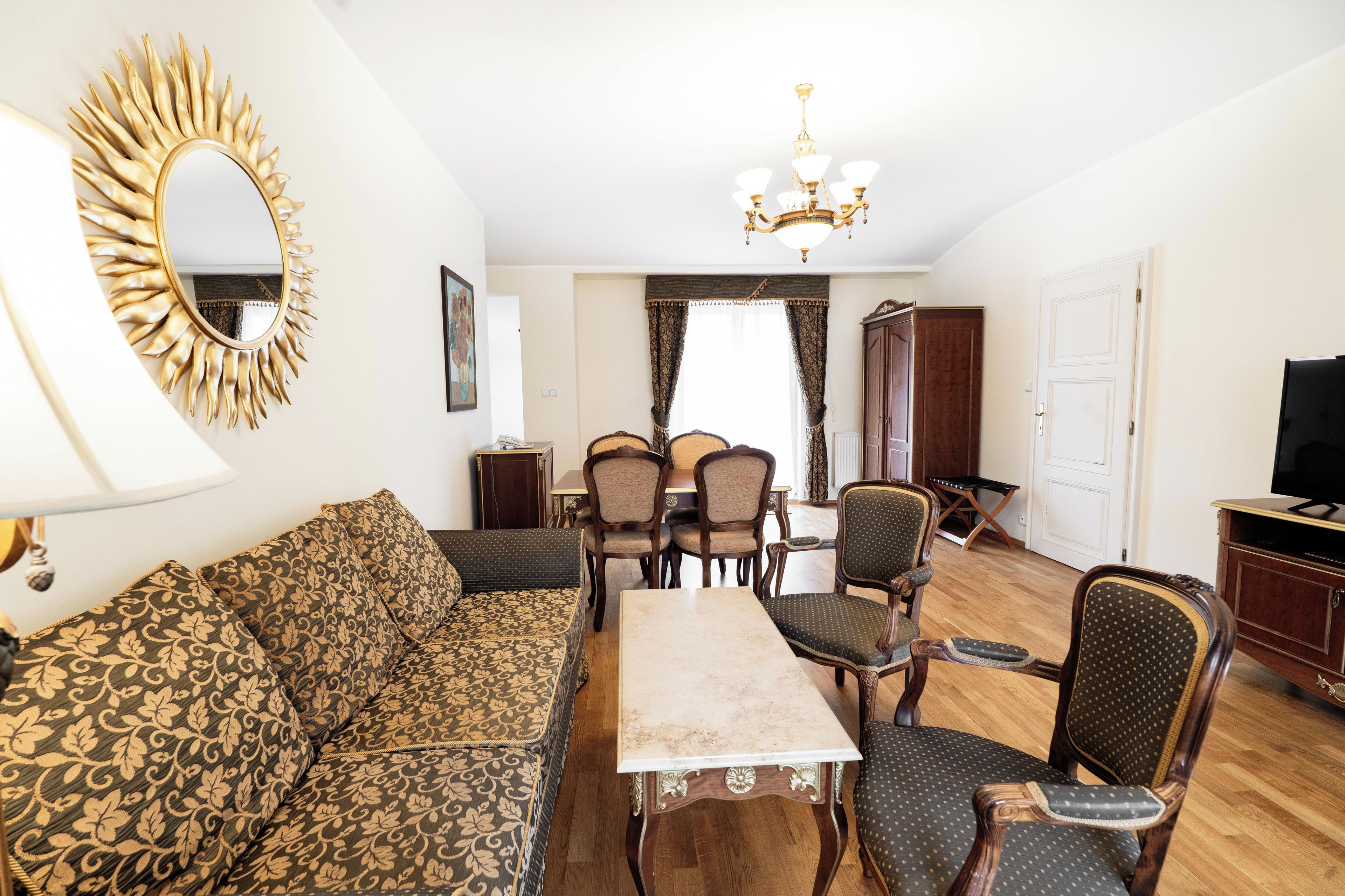 A living room with a sofa, dining table, chairs, a chandelier, and a television.