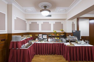 Disposição de buffet com diversos alimentos e um espaço para bebidas, em um salão com painéis de madeira e teto decorativo.