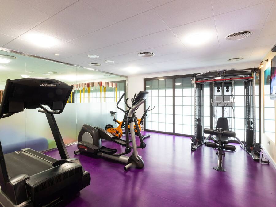 Un gimnasio con cintas de correr, elíptica y máquina de pesas.