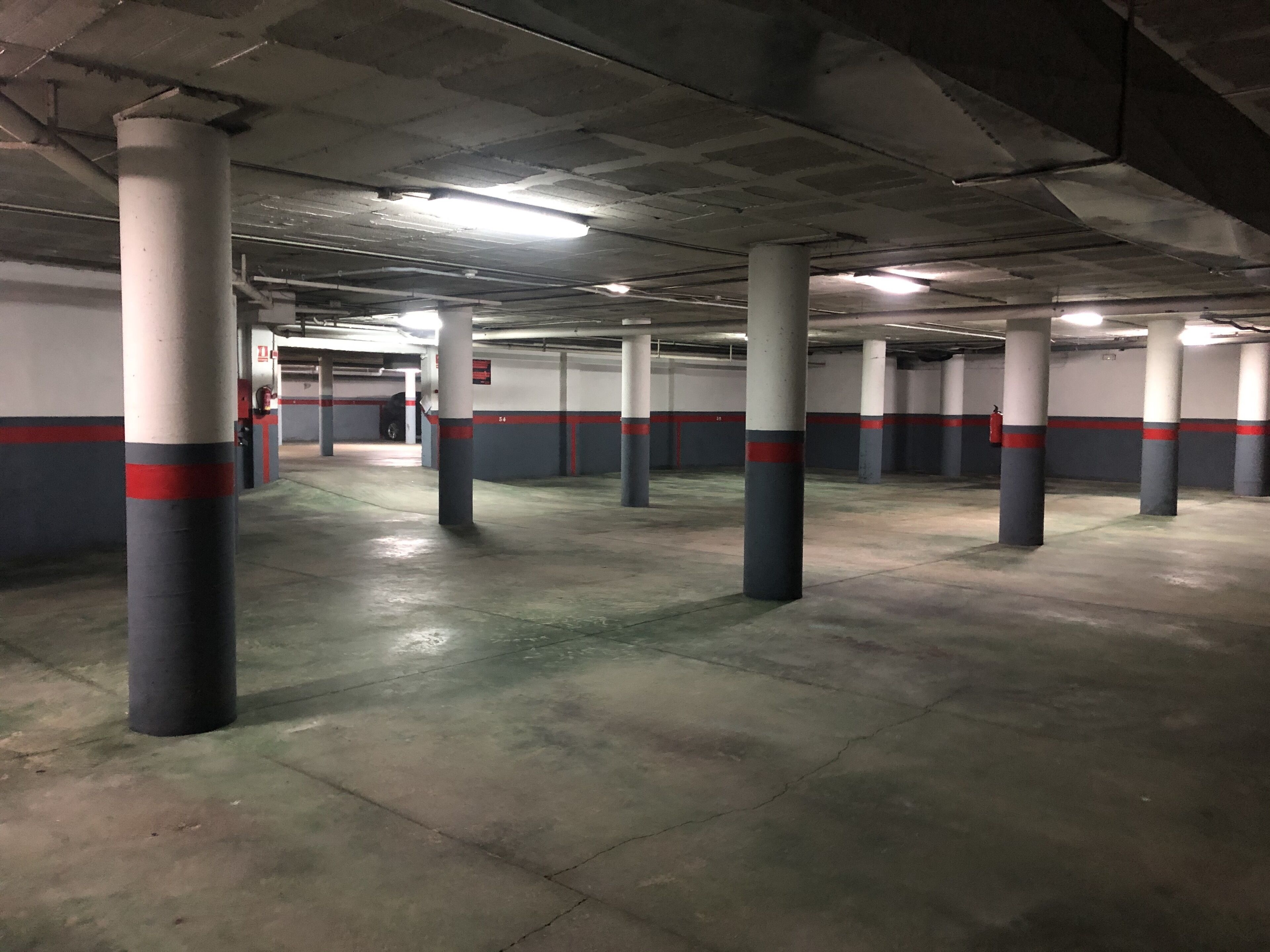 A parking garage with concrete pillars, fluorescent lighting, and a clean, empty floor.