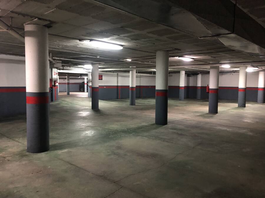 Un aparcamiento con pilares de hormigón, iluminación fluorescente y un suelo limpio y vacío.