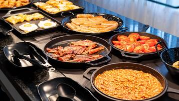 Un bufé con diversos platos, como huevos, tocino, salchichas, tomates y papas al horno.
