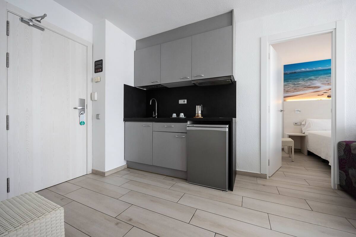 A compact kitchen with grey cabinets, a black countertop, and a built-in dishwasher.
