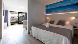 A modern hotel room with a large bed, a painting of a beach scene, and a balcony with outdoor furniture. - Aparthotel Miami Park (Calella)