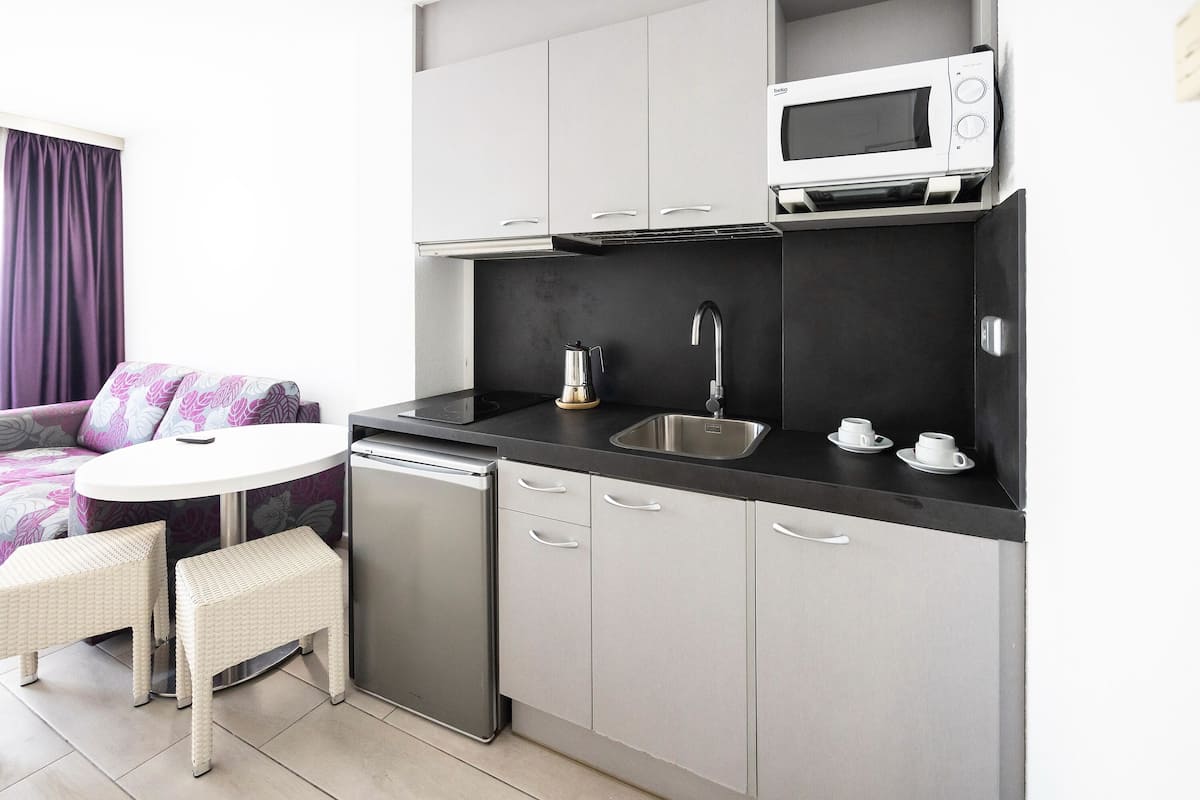 A compact kitchen with a microwave, sink, and two white wicker stools.