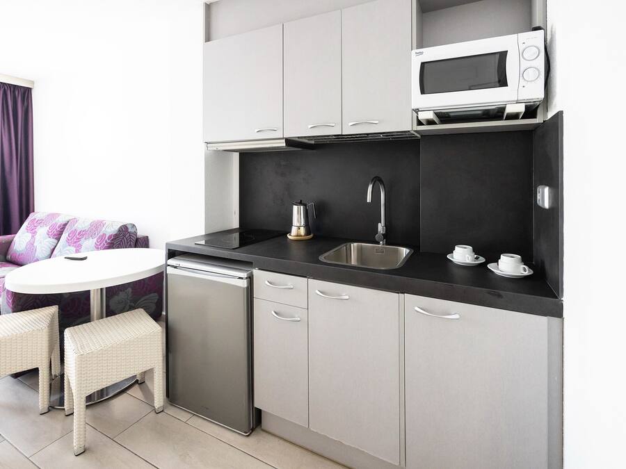 A compact kitchen with a microwave, sink, and two white wicker stools.