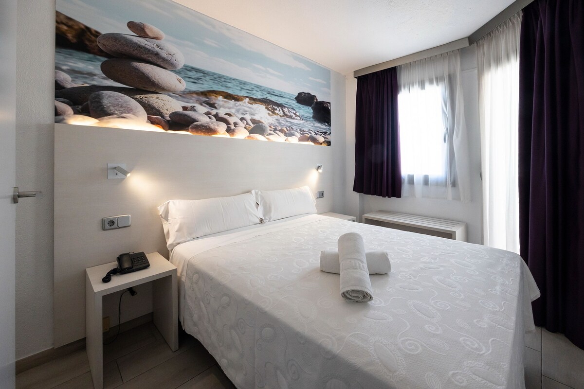 A neatly made bed with a rolled towel, a bedside phone, and a nightstand.