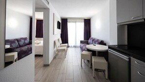 A modern hotel room with a kitchenette, two sofas, a dining table, and a large window with curtains. - Aparthotel Miami Park (Calella)