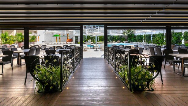 An outdoor dining area with a wooden deck, black metal railings, and potted plants. - Aparthotel Miami Park (Calella)