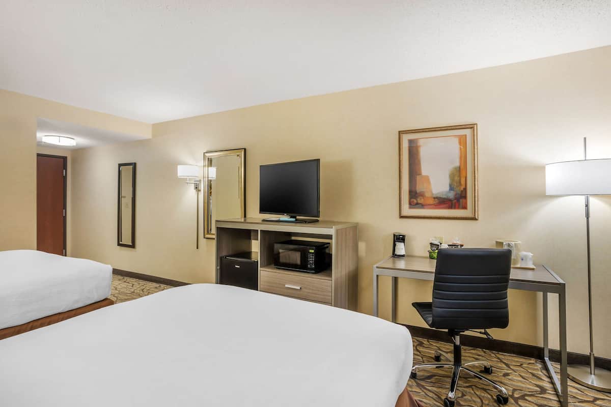 Habitación de hotel con dos camas, un escritorio con computadora, televisión, microondas, cafetera y una silla.