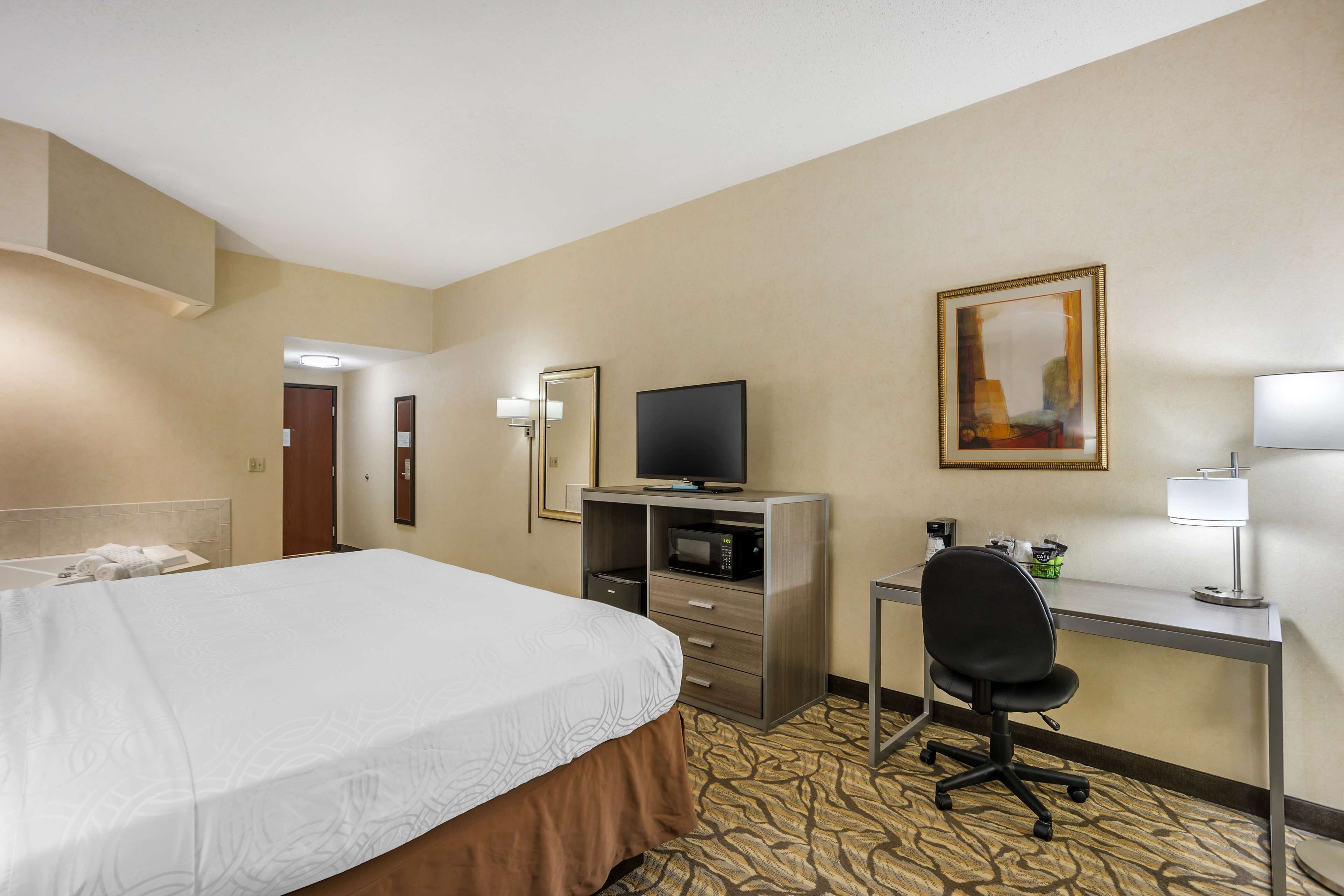 A hotel room with a bed, desk, chair, television, and a painting on the wall.