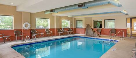 A pool area with chairs and a lifeguard chair, large windows, and a ceiling vent.