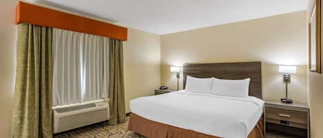 A hotel room with a large bed, two bedside tables with lamps, a window with curtains, and a patterned carpet.